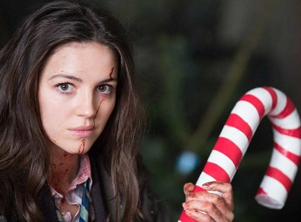 Anna with blood on her face holding a candy cane decoration as a weapon