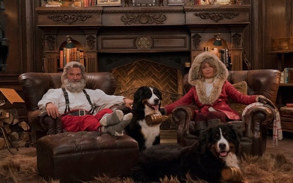 The Christmas Chronicles Santa and Mrs. Clause sitting in front of the fireplace with their dogs.